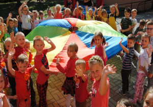 dzieci ustawione wg kolorów chusty i ubrań stoją na tarasie przedszkolnym i machają rękami